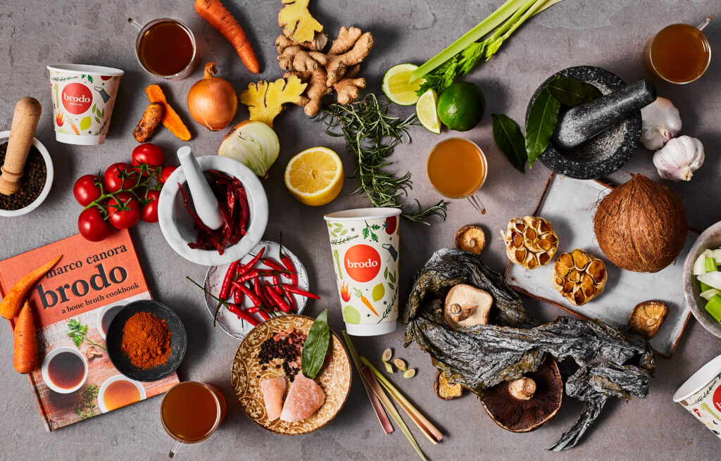 Brodo broth ingredients individually placed on a table with the Brodo logo in the middle on a paper cup.